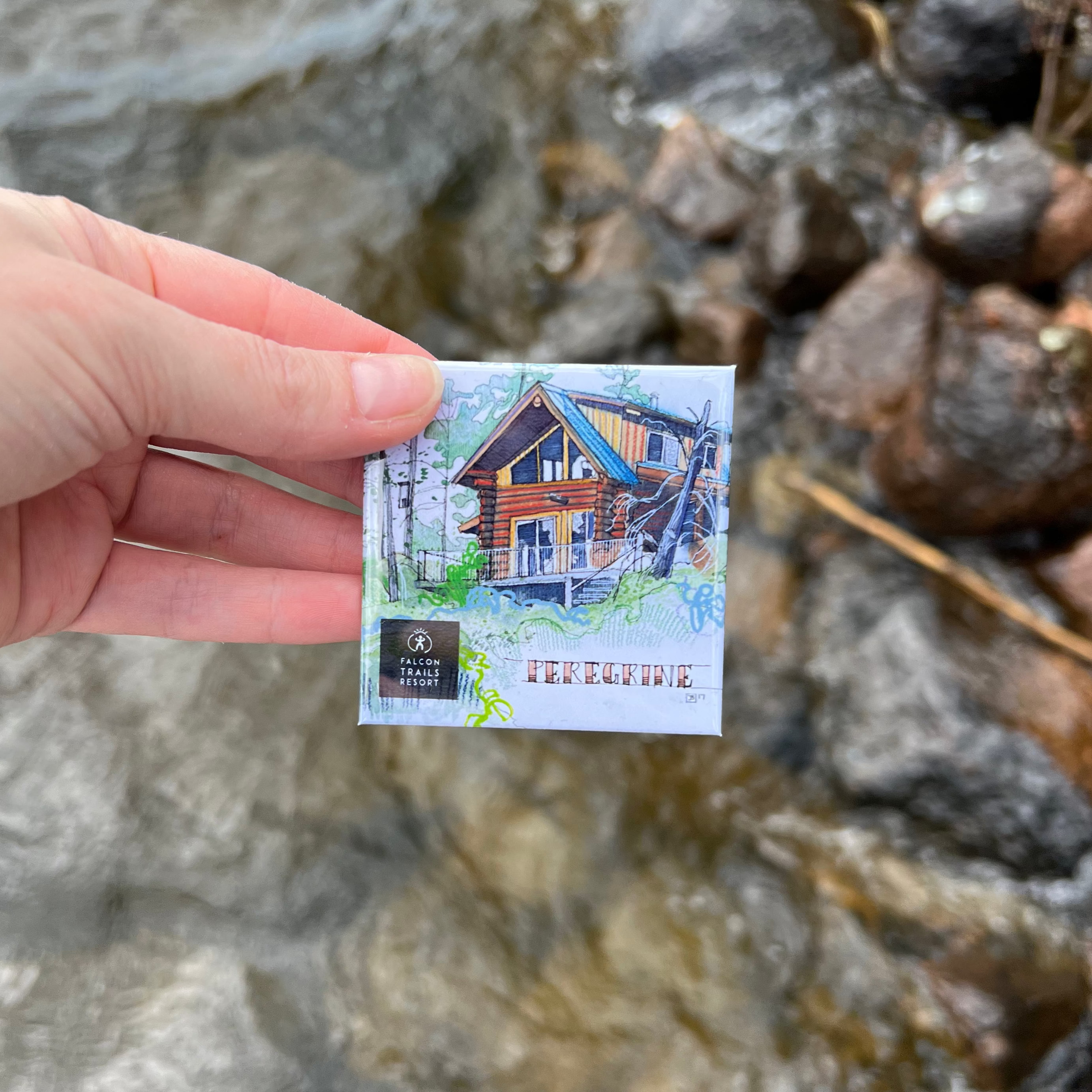 Hand holding a small custom corporate fridge magnet showing a logo against a natural background.